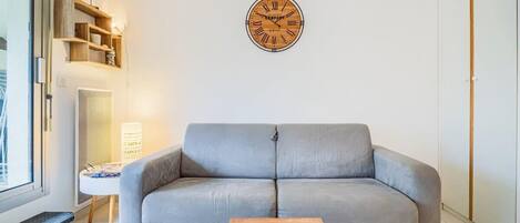 Een moderne woonkamer met een grijze bank, een houten salontafel, een wandklok en een boekenkast.