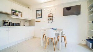 A modern kitchen with white cabinets, a dining table with chairs, a coffee maker, and a flat-screen TV mounted on the wall. - Vacances à pied studio charmant à 1min des plages (Carnac)
