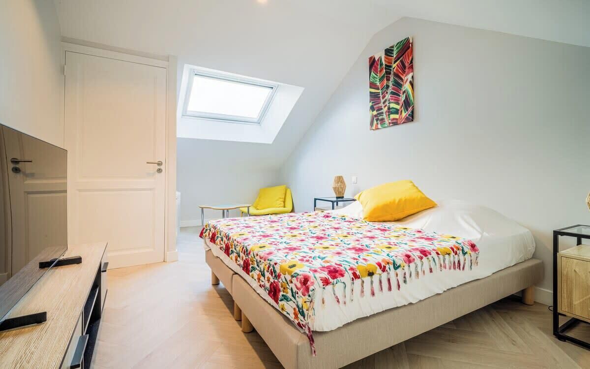 A bedroom with a bed, a desk, a chair, a window, and a painting on the wall.