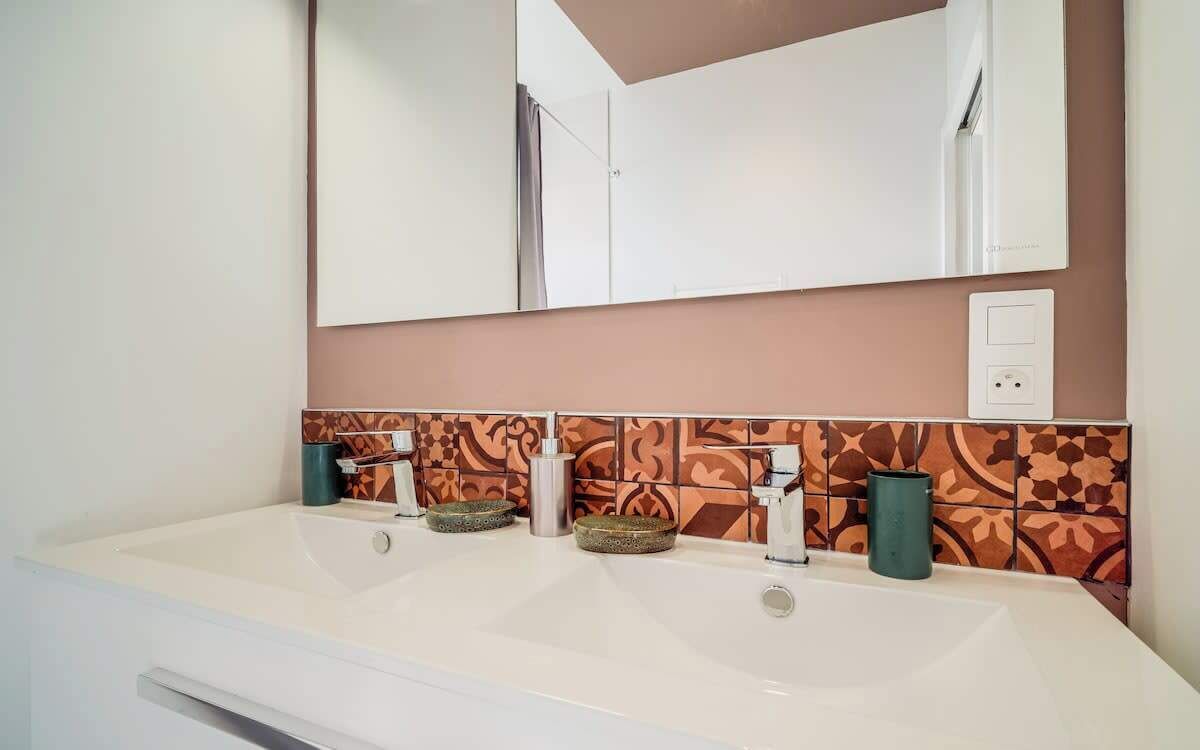 Une salle de bain avec un double lavabo, un miroir et des carreaux décoratifs sur le mur.