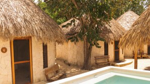 Zona de piscina amb cabanes de teules, una panxa de fusta i una paret de pedra.