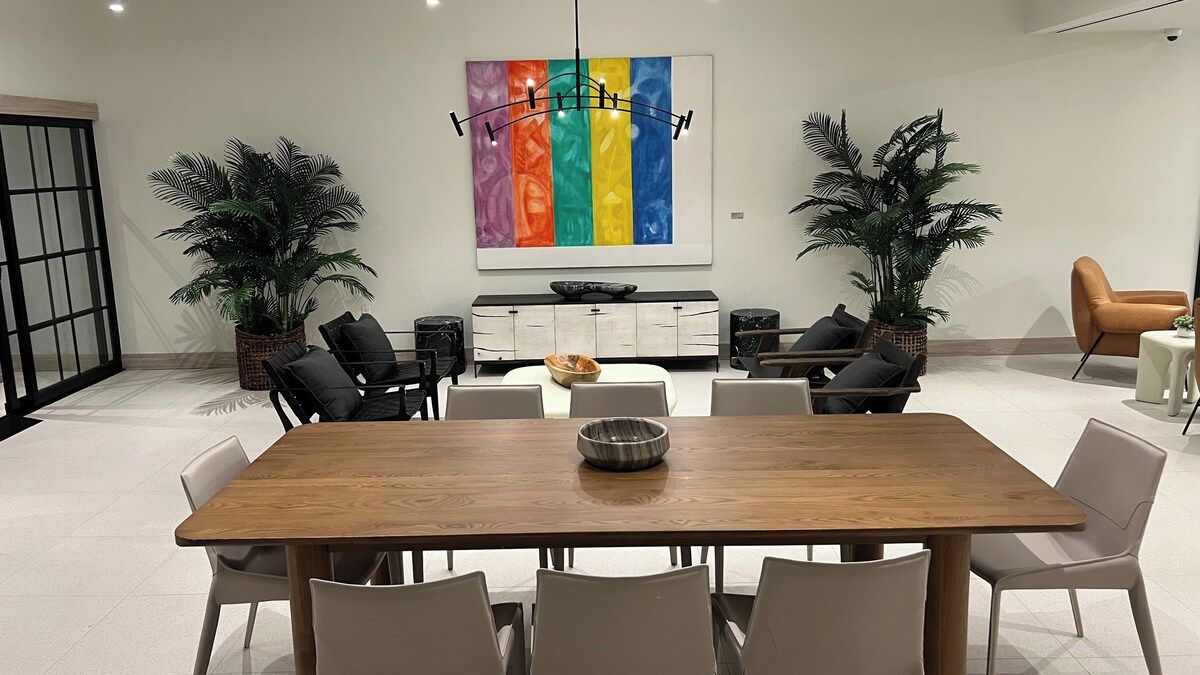 A modern dining area with a wooden table, white chairs, a buffet cabinet, and two potted plants.