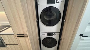 Una unidad compacta de lavadora y secadora en una cocina moderna con armarios de madera y una puerta de vidrio.