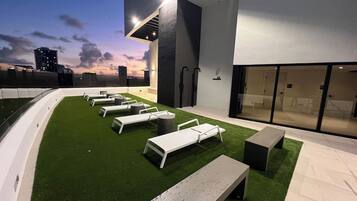 A rooftop lounge area with white lounge chairs and a small pool.