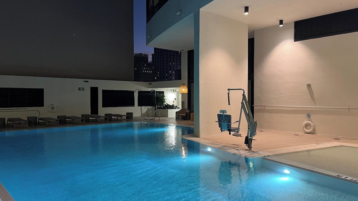 An indoor swimming pool with a diving board, lounge chairs, and a staircase leading to an upper level.