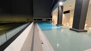 An indoor swimming pool with clear lane markings, a diving board, and lounge chairs.