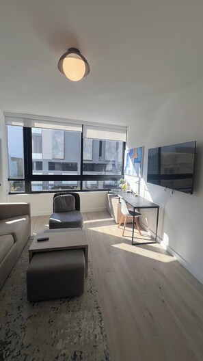 Una sala de estar moderna con un sofá, un reposapiés, una mesa de comedor, sillas y un televisor montado en la pared.