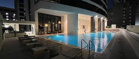 Un área de piscina en la azotea con sillones de descanso y un spa con paredes de vidrio.