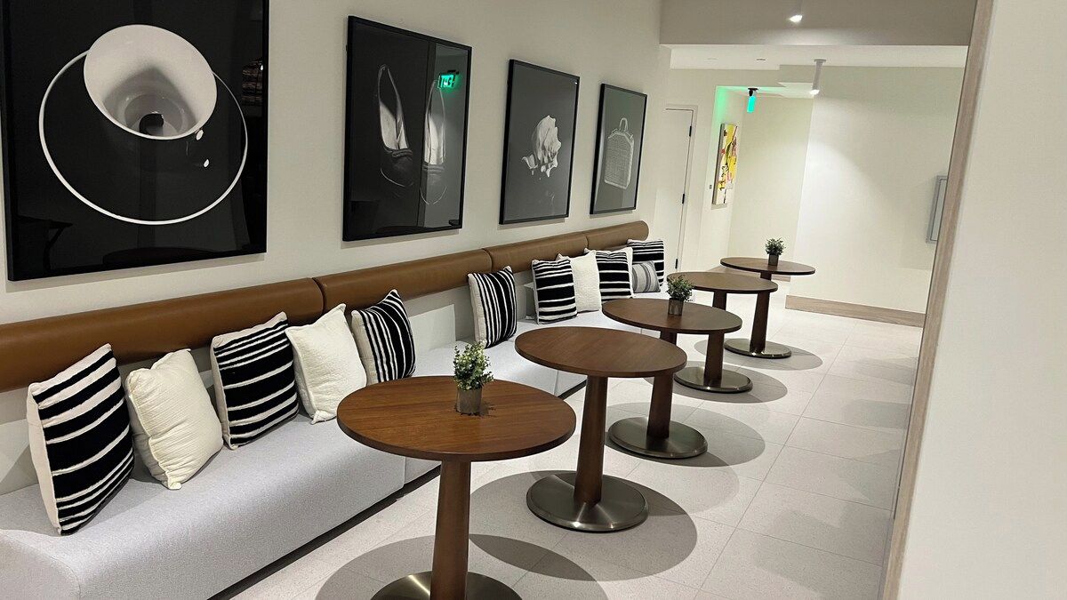 A modern hotel lobby with a sofa, multiple round tables, and framed artwork on the wall.