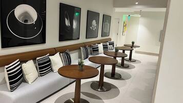 A modern hotel lobby with a sofa, multiple round tables, and framed artwork on the wall.