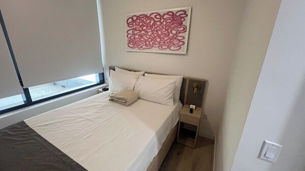 A hotel room with a bed, a bedside table, a wall-mounted artwork, and a window.