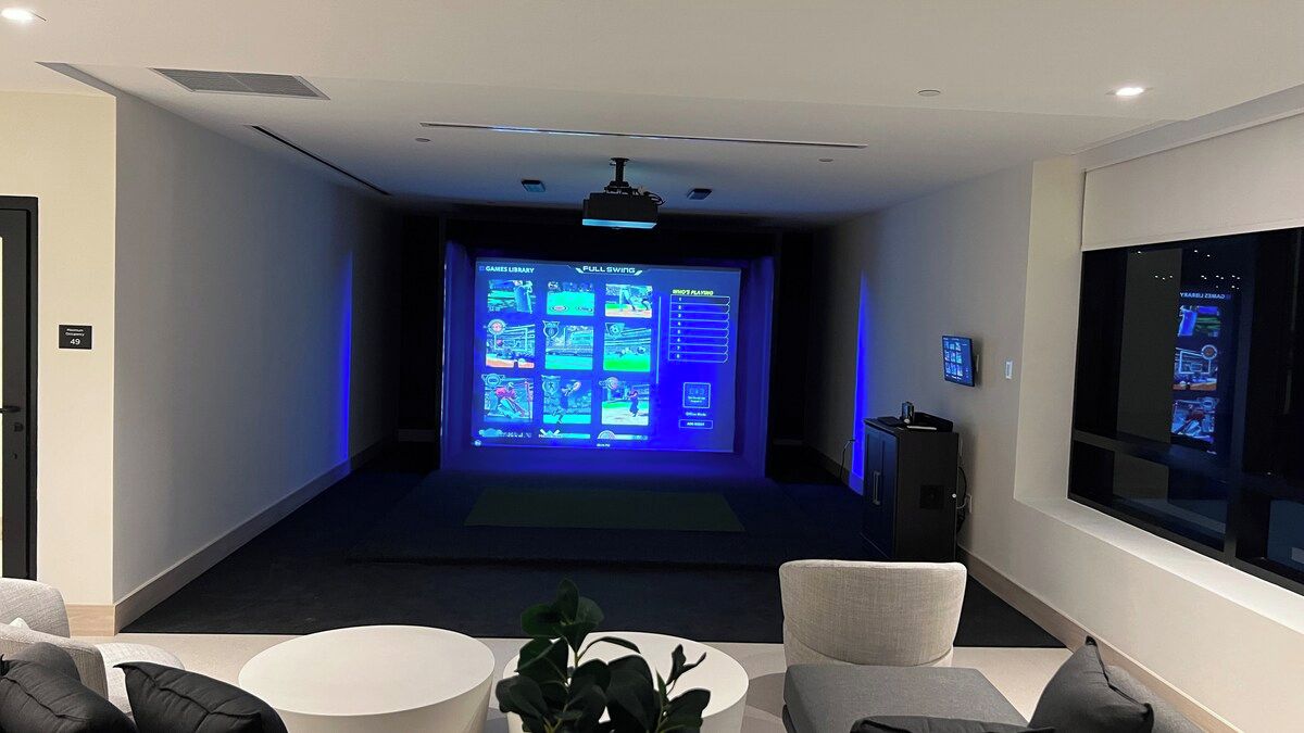 A modern room with a large screen displaying a presentation, a small table with a plant, and a seating area with chairs.