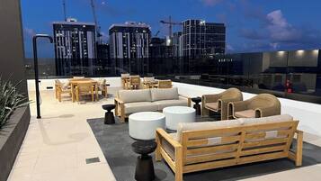 A rooftop terrace with outdoor seating, including sofas and chairs, and a view of the cityscape.