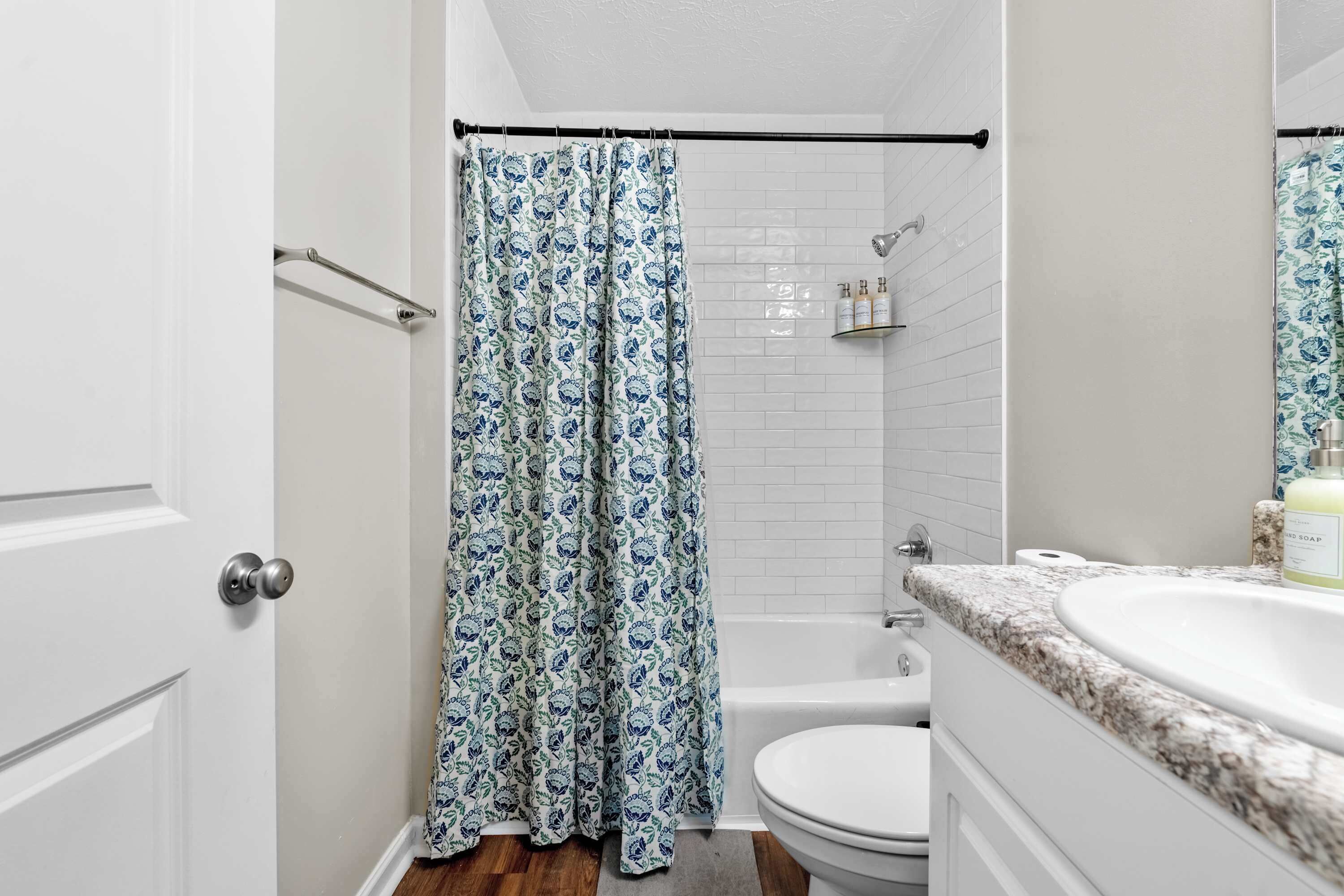 A bathroom with a shower curtain, a bathtub, a toilet, and a sink with a marble countertop.