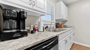Una cucina moderna con mobili bianchi, una macchina da caffè Keurig, una lavastoviglie e un piano di lavoro in granito.