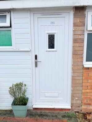 A white door with a small window, a sign above it, and a potted plant beside it. - EasyStay Studio-Modern 2 Bedroom Family Studio Near M1, Airport & Train Station (Luton)