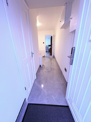A hallway with white doors, a black doormat, and a kitchen visible in the distance. - EasyStay Studio-Modern 2 Bedroom Family Studio Near M1, Airport & Train Station (Luton)
