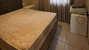 Una stanza con un letto, un condizionatore, una scrivania, una sedia e un comodino con una lampada.