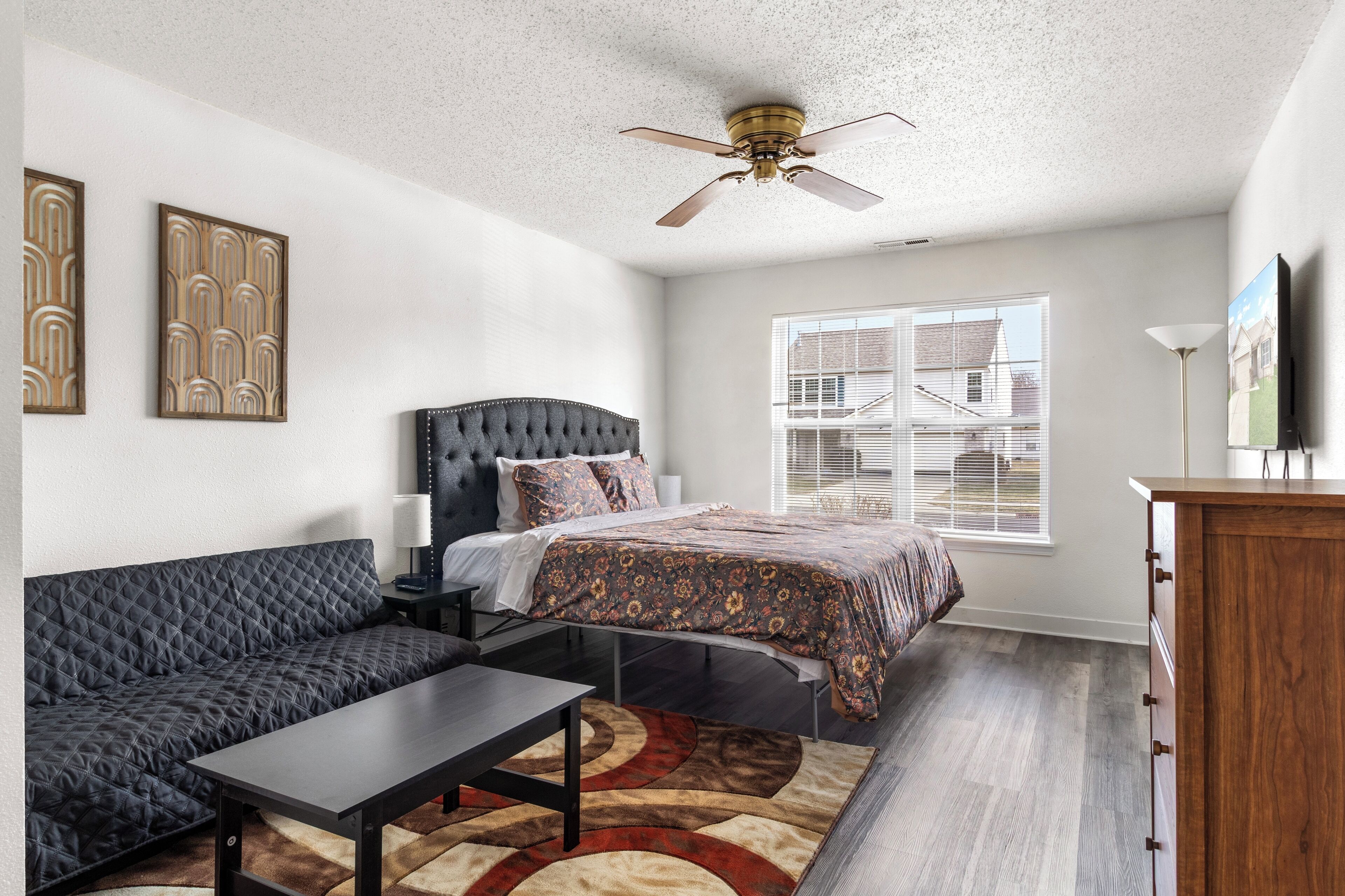 A bedroom with a bed, a sofa, a desk, a dresser, and a ceiling fan.