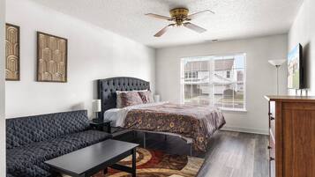 A bedroom with a bed, a sofa, a desk, a dresser, and a ceiling fan.