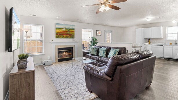 A spacious living room with a fireplace, a ceiling fan, and a kitchen area in the background. - Quiet Stay w Workspace, Fast Wi-Fi & Parking (Fishers)