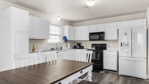 A modern kitchen with white cabinetry, a wooden dining table, and a black microwave. - Quiet Stay w Workspace, Fast Wi-Fi & Parking (Fishers)