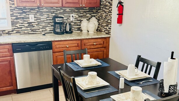 A modern kitchen with wooden cabinets, a stone backsplash, and a dining area with a dark wooden table set for four.