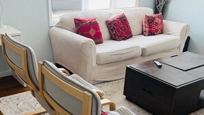 A living room with a white sofa, two wooden chairs, a coffee table, and a TV stand.