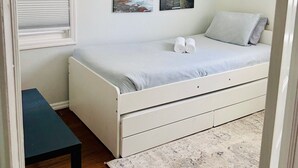 A bedroom with a bed, a window with blinds, a radiator, and two wall-mounted pictures.