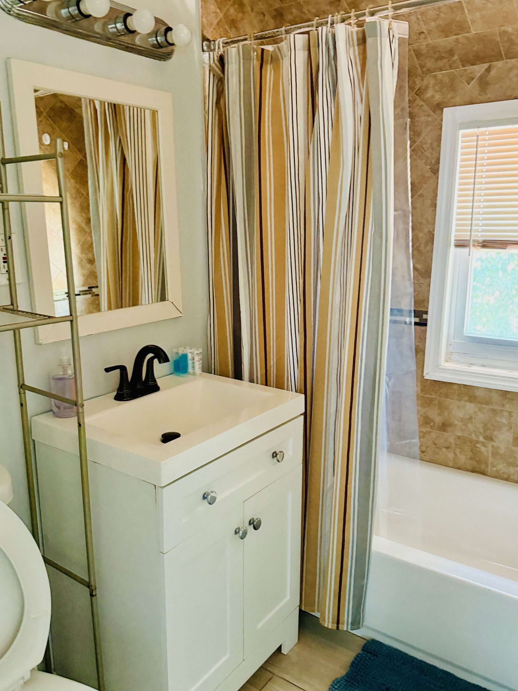 Un bagno con un lavandino bianco, uno specchio, una tenda da doccia e una finestra.