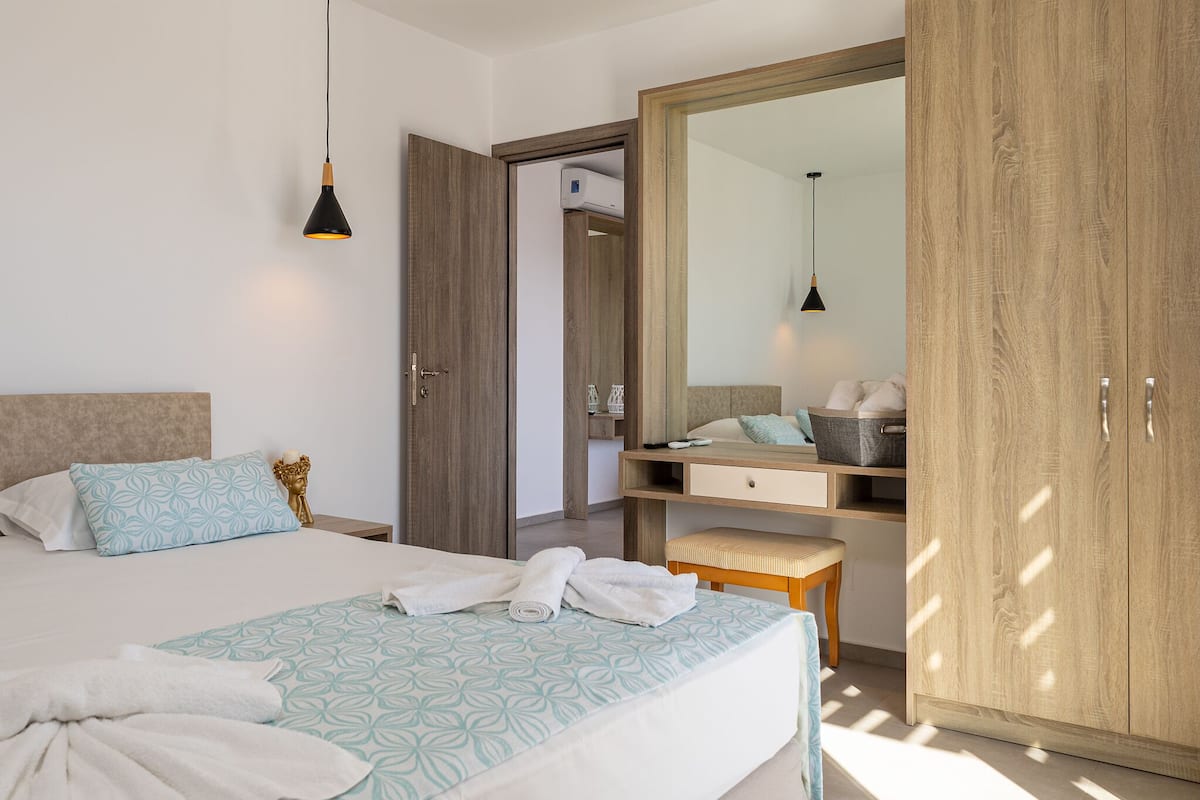 Moderni hotellihuone, jossa on suuri sänky, puinen vaatekaappi, työpöytä tuolilla ja riippuvalaisin.