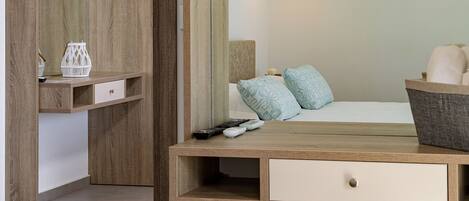 A bedroom with a wooden desk, a bedside table, a chair, a bed, and a hanging light fixture.