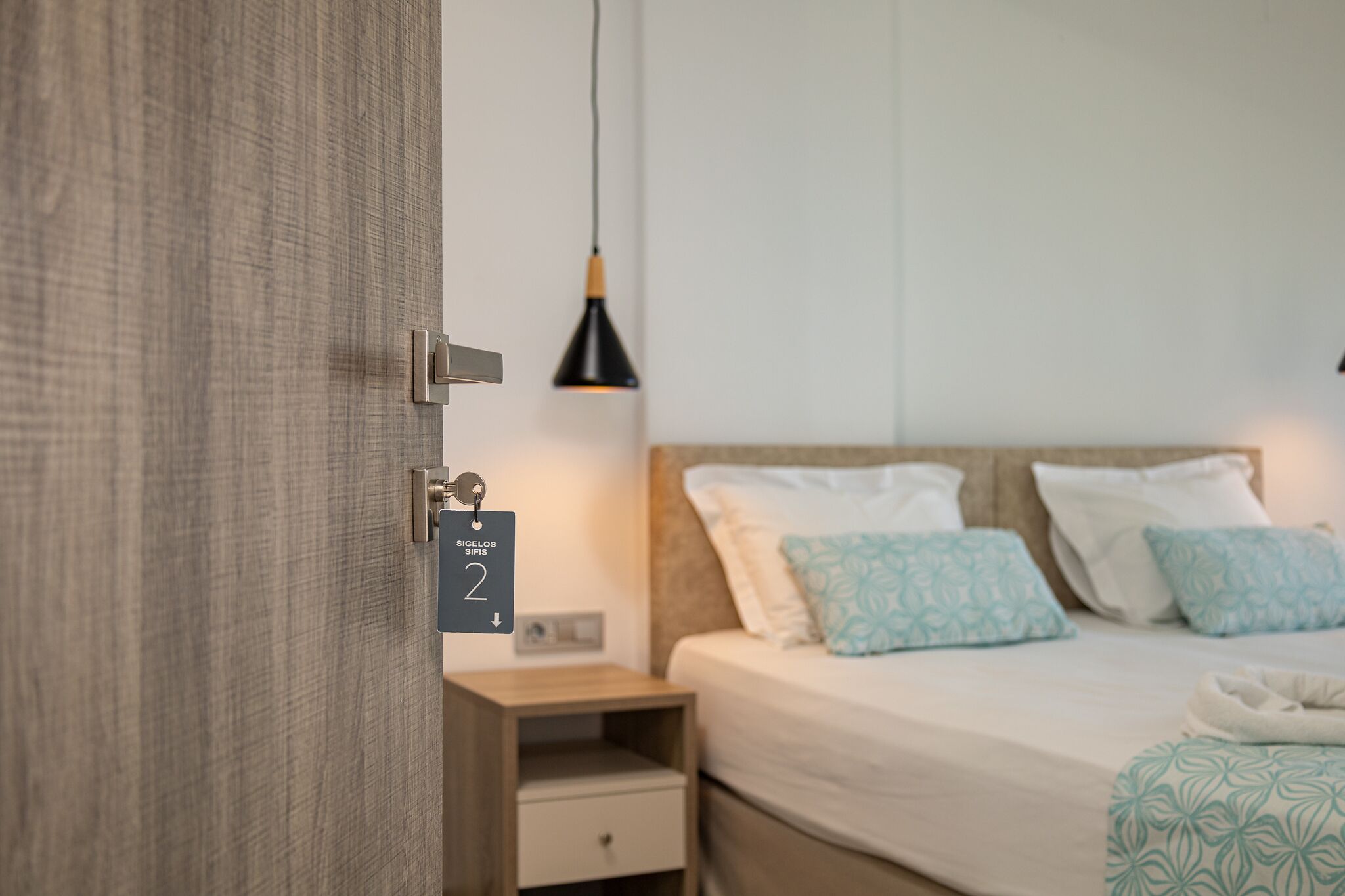 Una camera d'albergo con un letto, un comodino, una lampada e una porta dotata di chiusura a chiave elettronica.