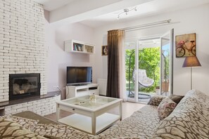 Ein Wohnzimmer mit Kamin, Fernseher, Glastisch, Sofa und Blick auf einen Balkon mit einem Fahrrad.