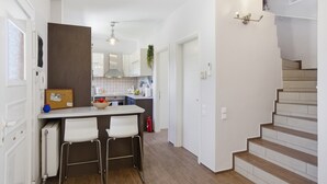 A modern kitchen with white cabinets, a central island, and a staircase leading to an upper floor. - Euphoria Country House with Jacuzzi and Barbecue (Agios Ioannis)