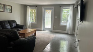 Ein Wohnzimmer mit einer schwarzen Ledersofa, einem Holztisch und zwei Fenstern mit weißen Vorhängen.