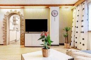 Ein Wohnzimmer mit Flachbildfernseher, Zimmerpflanze, einer Uhr und einem Steinbogen.