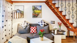 Un salon comprenant un canapé, une table basse, un escalier et deux tableaux accrochés au mur.