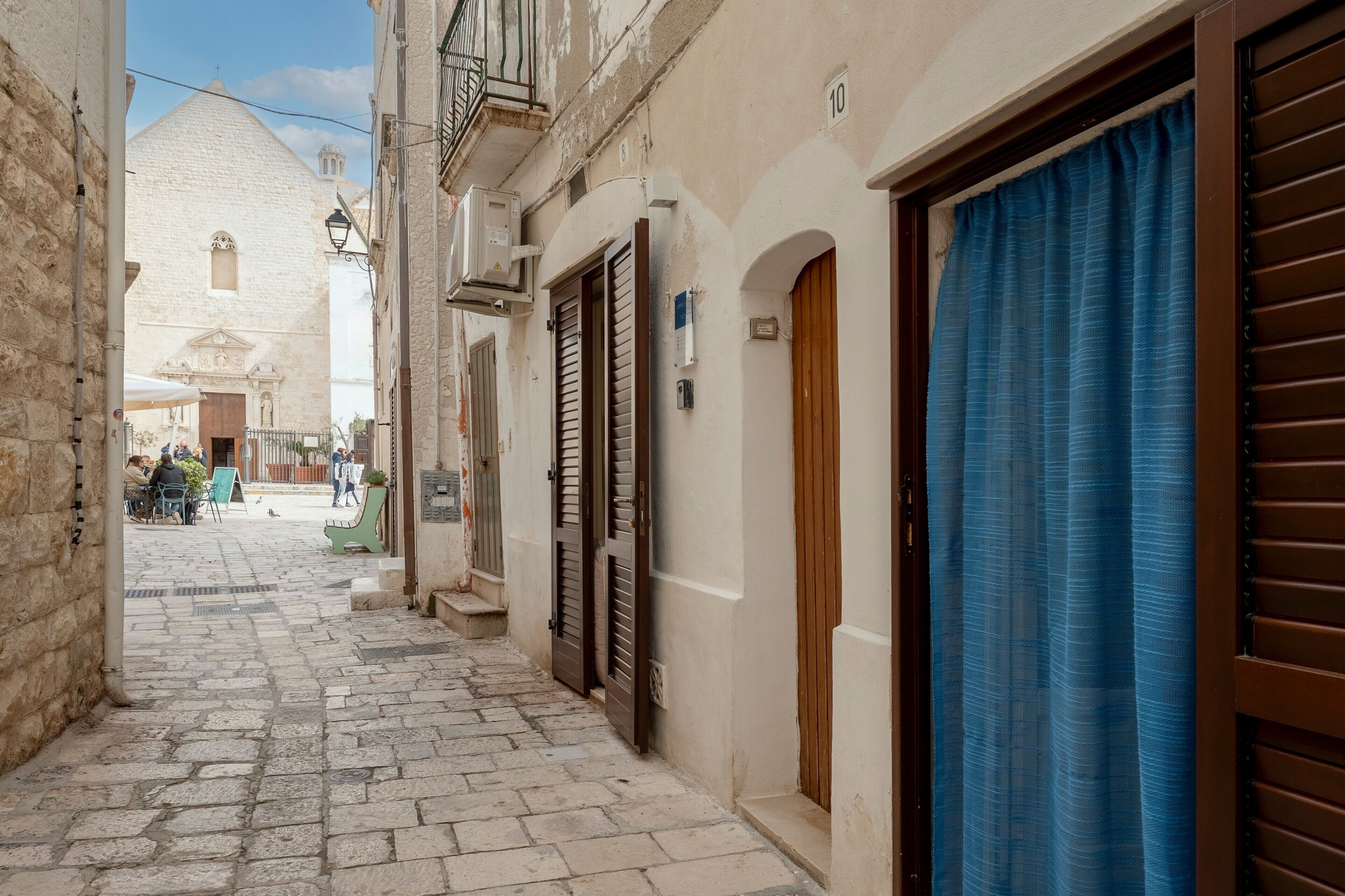 Una calle estrecha con pavimento de piedra, edificios con contraventanas de madera y una cortina azul a un lado.