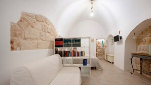 Een kamer met een witte bank, een boekenkast, een stenen muur en een kleine tafel.