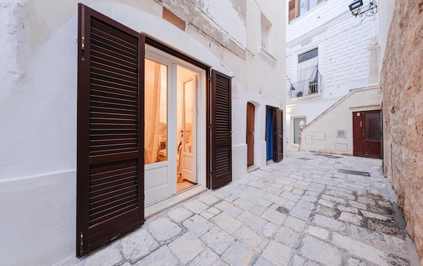 Une ruelle étroite, pavée de pierres, bordée de bâtiments de chaque côté, dont les fenêtres sont dotées de volets en bois.