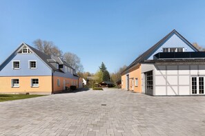 Une cour spacieuse avec un chemin pavé, deux bâtiments aux styles architecturaux différents et un ciel dégagé.