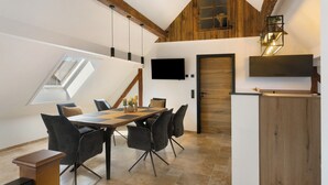 A dining area with a table, chairs, and a TV mounted on the wall. - Vogtlandstadl – Modern Lakeside Holiday Home in Vogtland, Spacious & Comfortable (Bad Brambach)