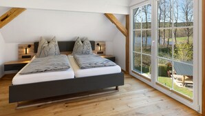 A bedroom with a bed, two bedside tables, a large window with a view of trees and a lake, and wooden beams on the ceiling. - Vogtlandstadl – Modern Lakeside Holiday Home in Vogtland, Spacious & Comfortable (Bad Brambach)