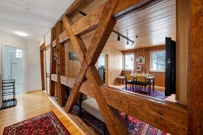 Quarto com vigas de madeira, sala de jantar com mesa e cadeiras, e vista para a cozinha.
