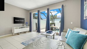 Ein modernes Wohnzimmer mit einer Couch, einem Couchtisch, einem Fernseher und Blick ins Freie.