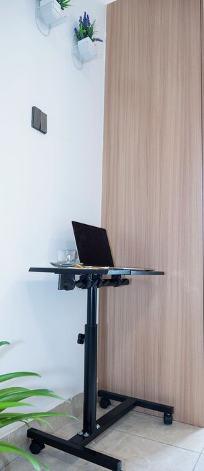 Ein Laptop auf einem schwarzen Rollgestell, ein Glas Wasser und eine kleine Pflanze an einer weißen Wand.