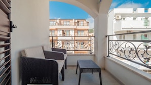 Un balcón con muebles de mimbre, vista a edificios cercanos y un cielo azul despejado.