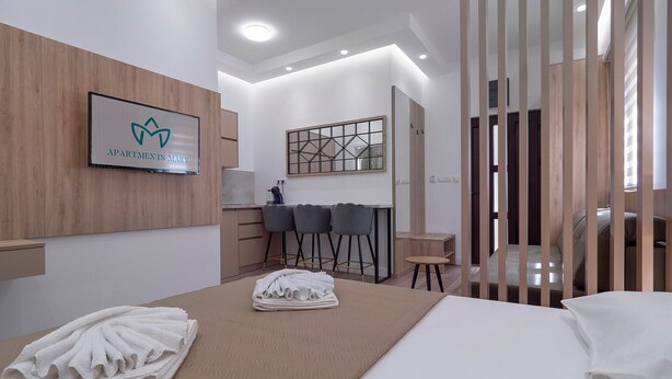 Una habitación de hotel moderna con una cama, un escritorio, dos sillas, una mesita y un televisor fijado a la pared.
