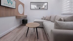 Una sala de estar moderna con un sofá, una mesa redonda de madera, un espejo y un cartel enmarcado en la pared.